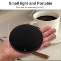 Someone holding the heating coaster next to a cup of coffee. Dimensions of 120mm in length and width, 7mm in depth.