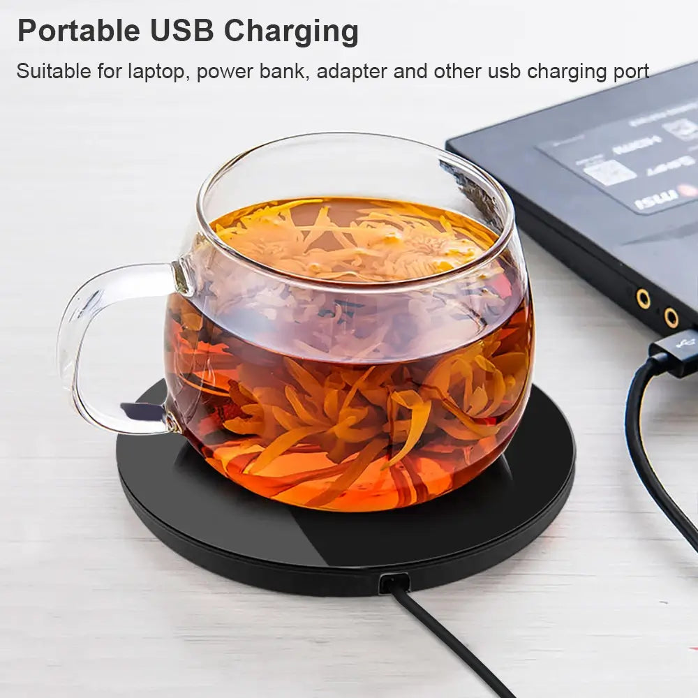 The electric mug warmer, heating up a cup of tea while it charges from a laptop using its USB charging cord.