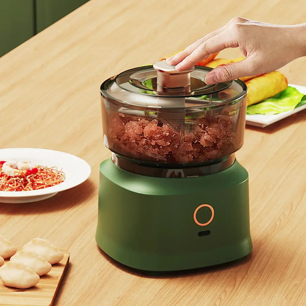 The mini electric meat grinder mincer machine in green, containing blended meat while someone pushes on the devices start button.